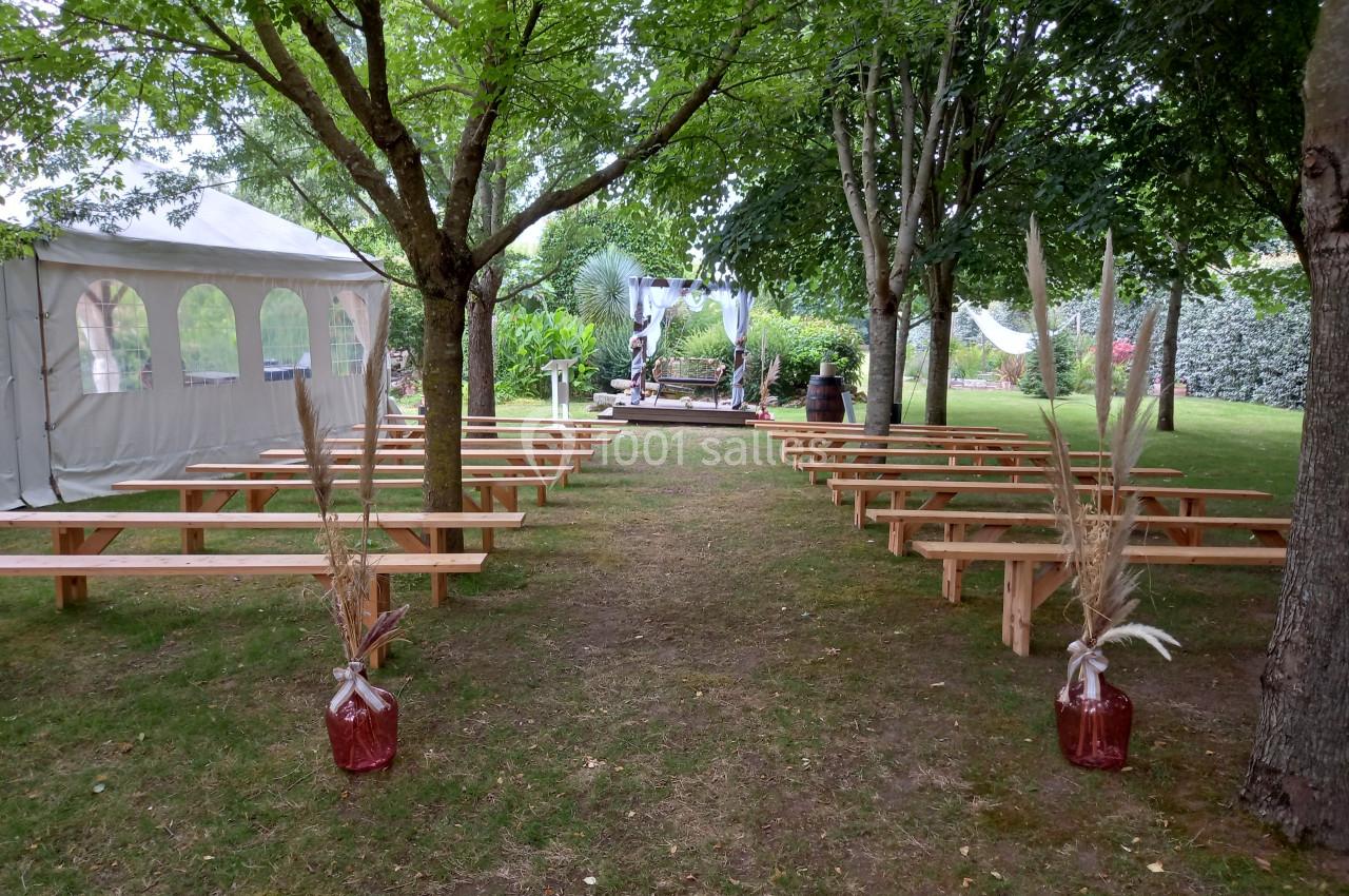 Allée centrale bordée de bancs en bois menant à une arche décorée, installée dans un jardin avec des arbres.