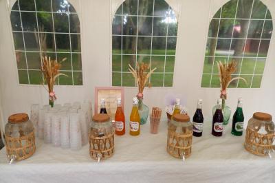 Deux balais déguisés en mariés avec robe et costume, posés devant une tente blanche et un cadre décoratif.