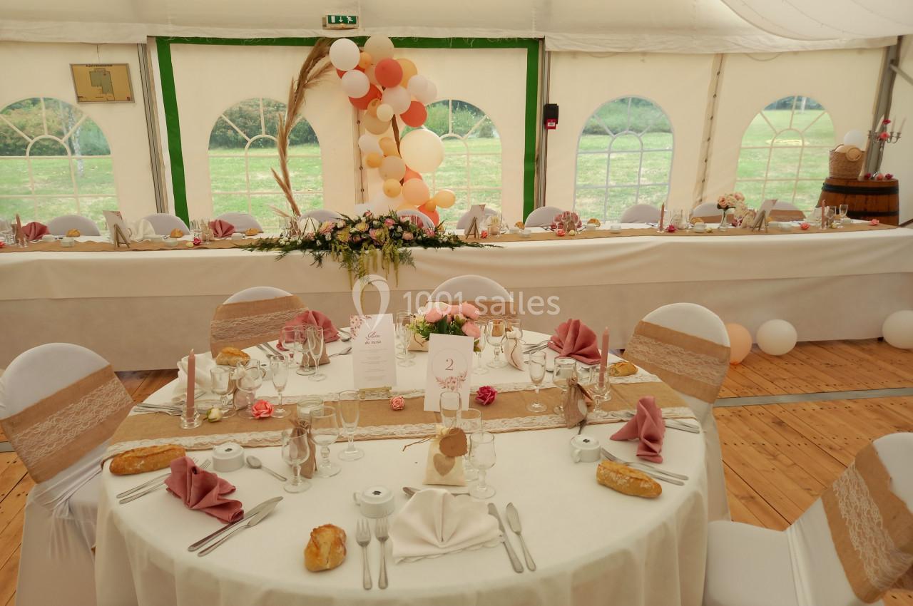 Salle de réception décorée pour un mariage avec tables dressées, nappes blanches, serviettes roses et centre de table floral.