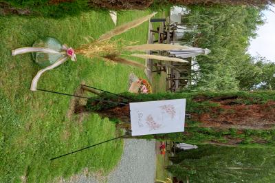 Deux balais déguisés en mariés avec robe et costume, posés devant une tente blanche et un cadre décoratif.