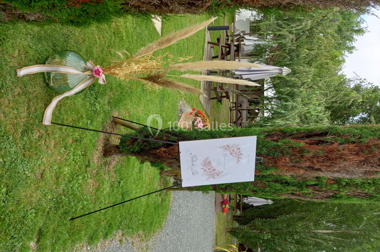 Panneau décoratif avec fleurs séchées et ruban, installé dans un jardin verdoyant près de tables et parasols.