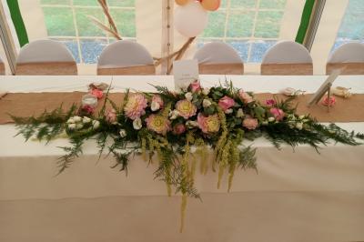 Deux balais déguisés en mariés avec robe et costume, posés devant une tente blanche et un cadre décoratif.