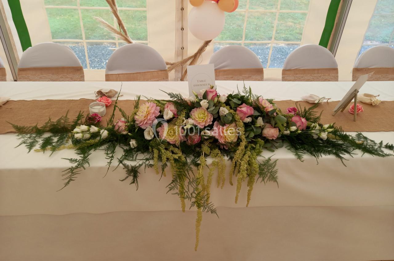 Décoration florale avec roses et feuillage sur une table blanche dans une salle de réception sous tente.