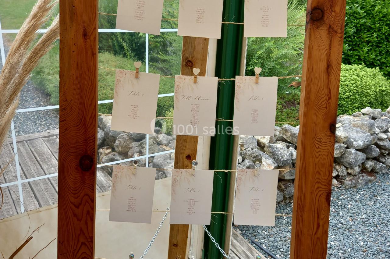 Cadre en bois vertical avec des cartes suspendues, affichant des noms ou des informations, dans un décor extérieur.