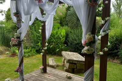 Deux balais déguisés en mariés avec robe et costume, posés devant une tente blanche et un cadre décoratif.