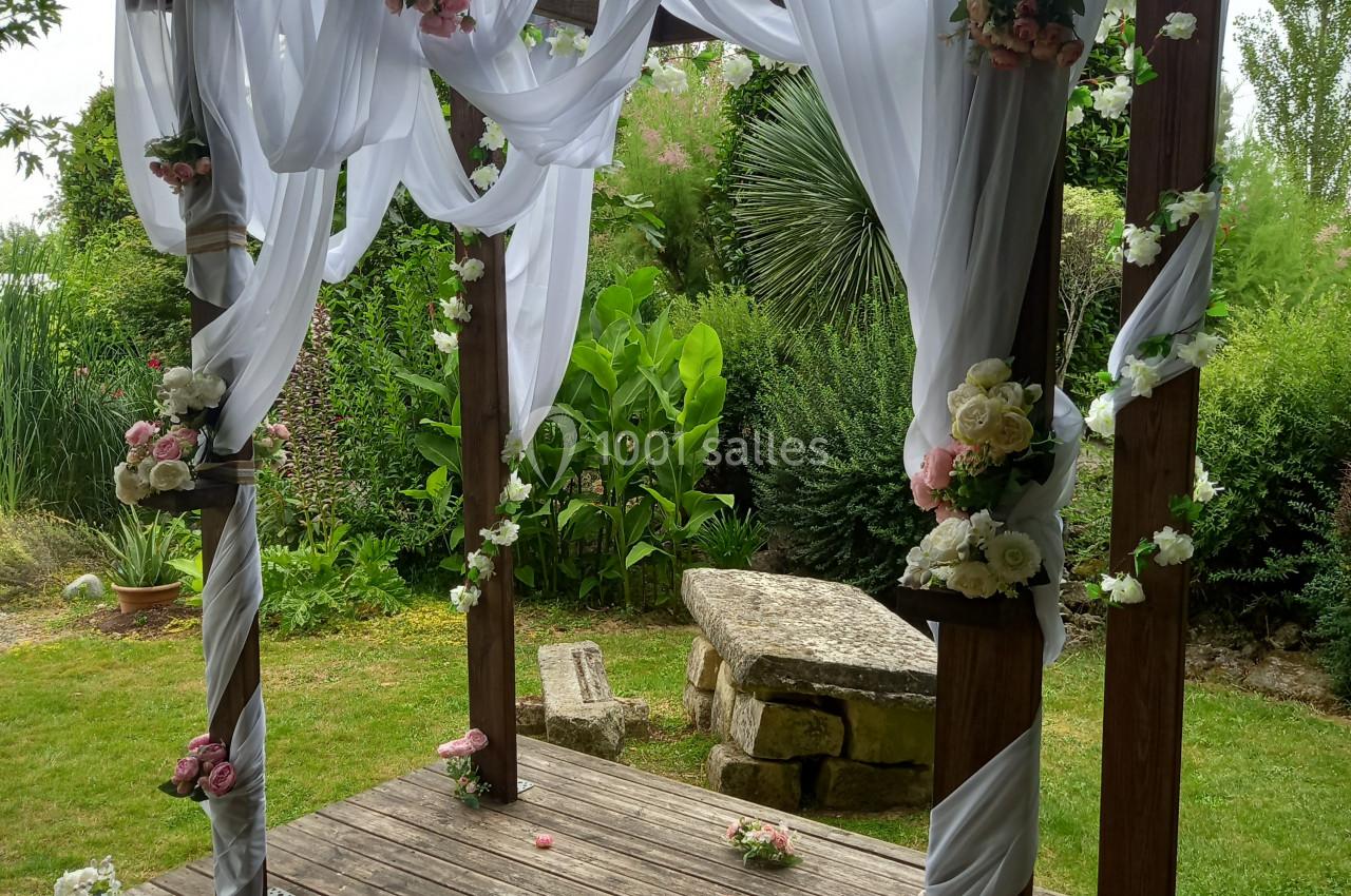 Structure en bois décorée de voilages blancs et de fleurs, installée dans un jardin verdoyant.