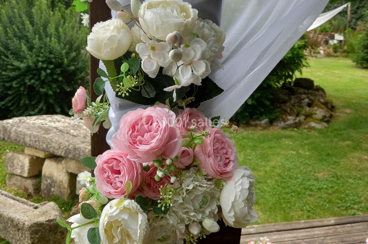Arrangement floral avec pivoines roses et blanches attaché à une structure en bois décorée de voilages blancs, en extérieur.