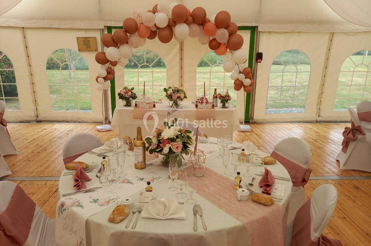 Salle de réception décorée pour un mariage avec tables dressées, nappes roses et arche de ballons dans une tente.