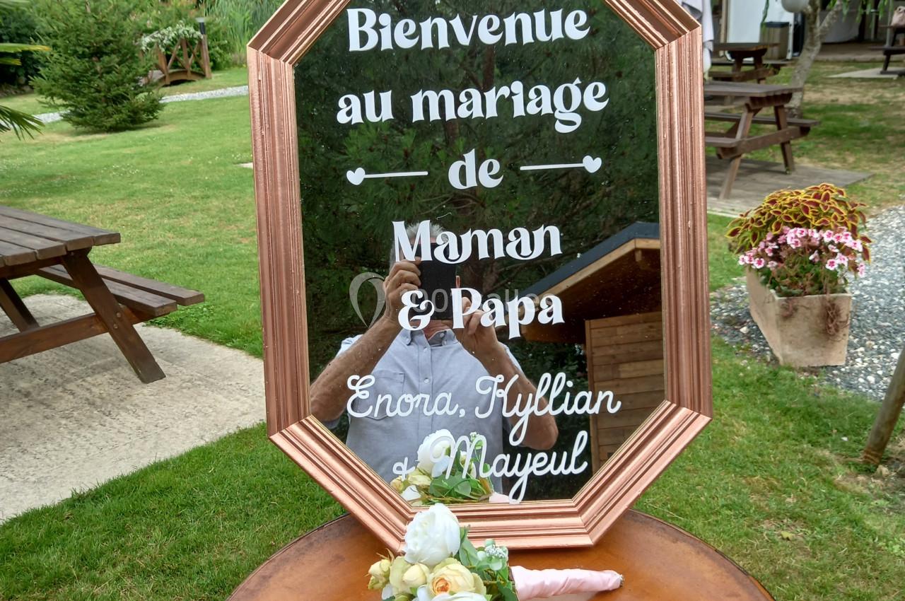 Panneau de bienvenue au mariage, posé sur un tonneau, avec des fleurs blanches, dans un jardin verdoyant.