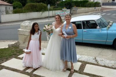 Deux balais déguisés en mariés avec robe et costume, posés devant une tente blanche et un cadre décoratif.