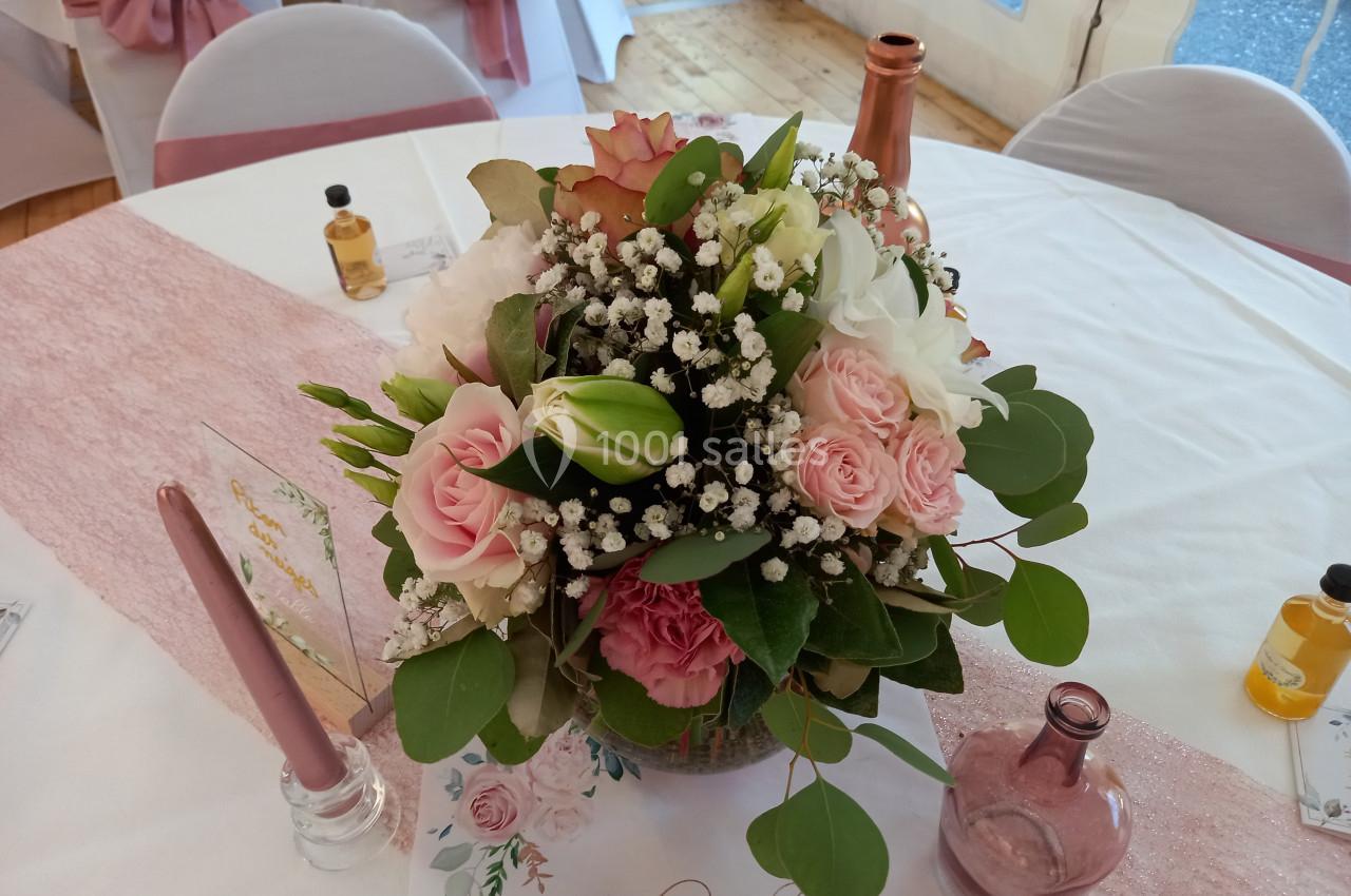 Bouquet de fleurs roses, blanches et vertes avec gypsophile, disposé sur une table décorée pour un événement.