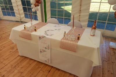 Deux balais déguisés en mariés avec robe et costume, posés devant une tente blanche et un cadre décoratif.