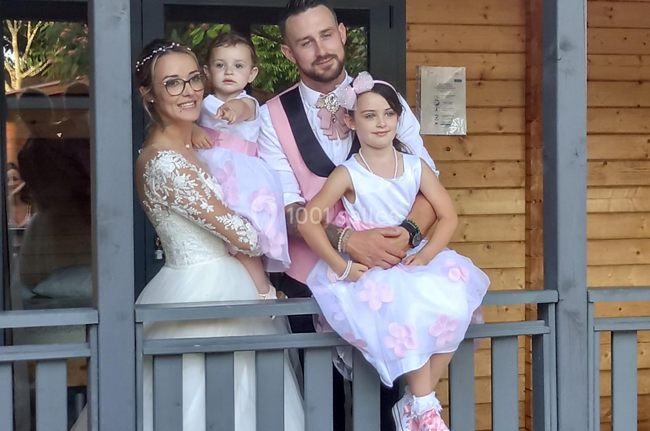 Une famille posant sur une terrasse en bois, les parents en tenue de mariage et les enfants en robes assorties.