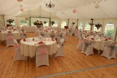 Deux balais déguisés en mariés avec robe et costume, posés devant une tente blanche et un cadre décoratif.