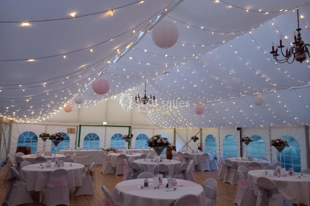 Salle de réception sous une tente avec des tables décorées, des guirlandes lumineuses et des lanternes suspendues.