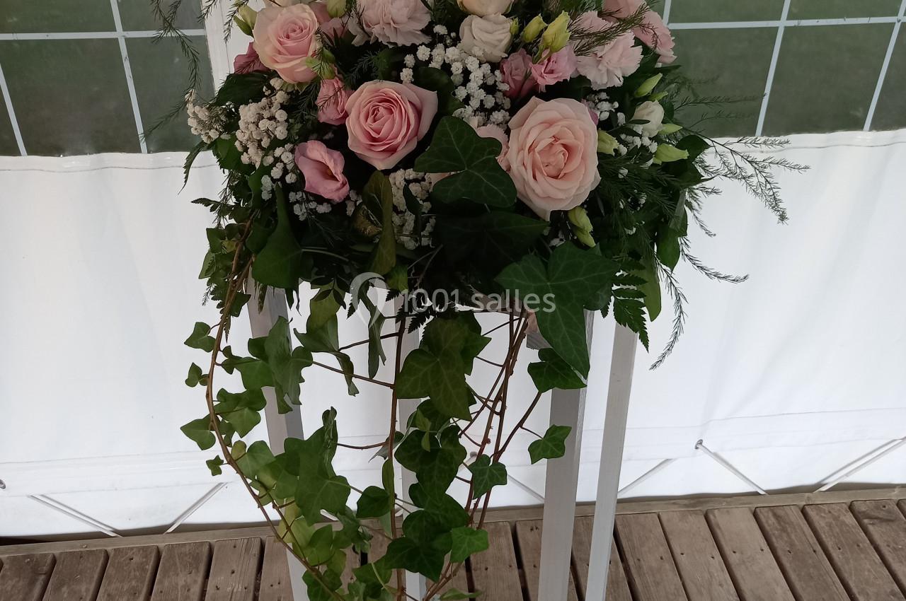 Arrangement floral avec des roses roses, du gypsophile et du lierre, posé sur un support blanc en bois sur une terrasse.