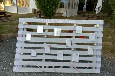 Deux balais déguisés en mariés avec robe et costume, posés devant une tente blanche et un cadre décoratif.