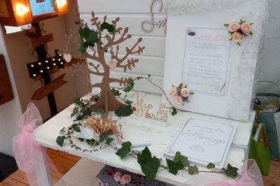 Deux balais déguisés en mariés avec robe et costume, posés devant une tente blanche et un cadre décoratif.