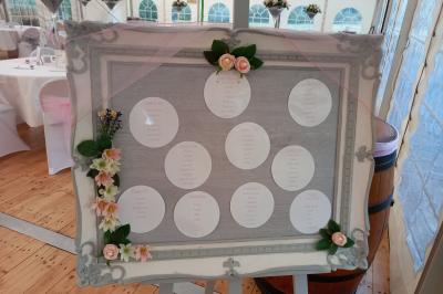 Deux balais déguisés en mariés avec robe et costume, posés devant une tente blanche et un cadre décoratif.