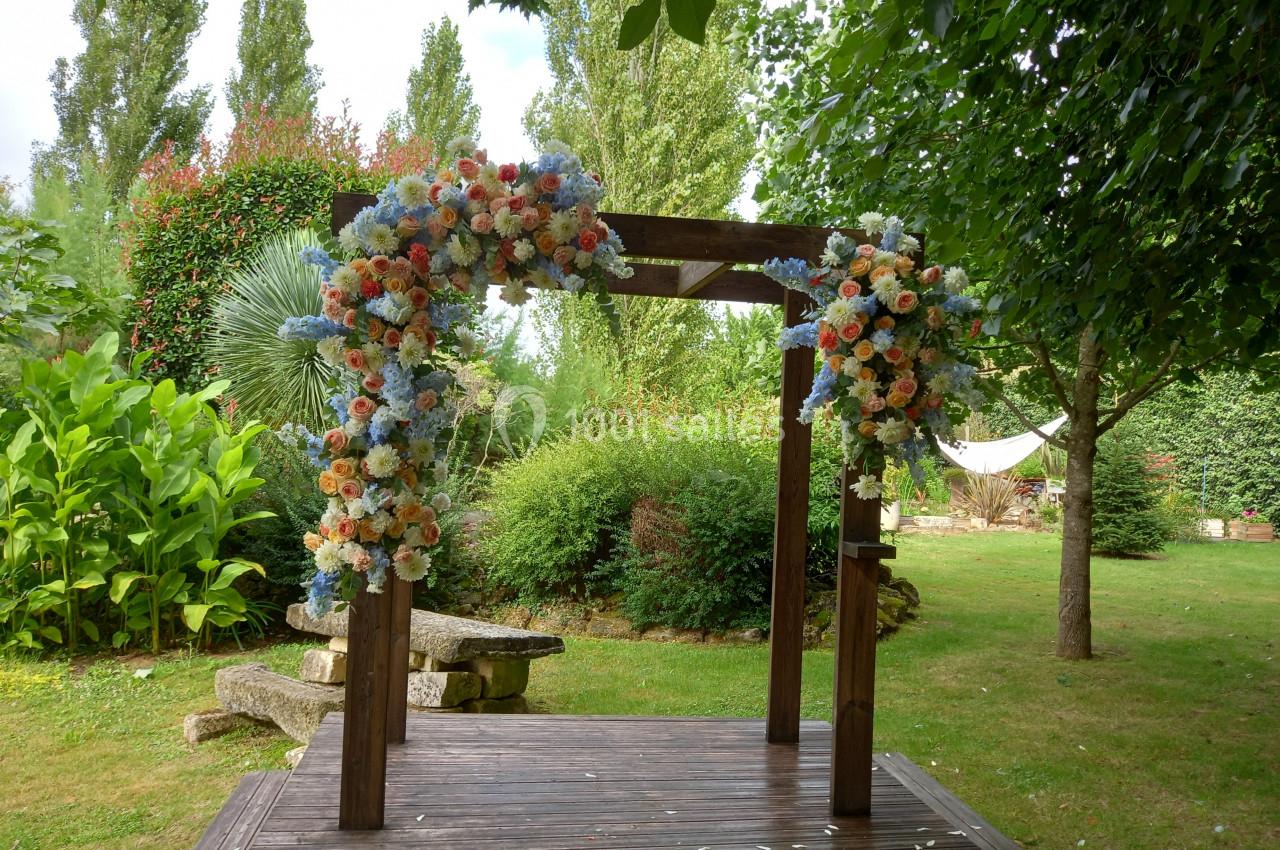 Structure en bois décorée de fleurs colorées dans un jardin verdoyant avec des arbres et des buissons en arrière-plan.