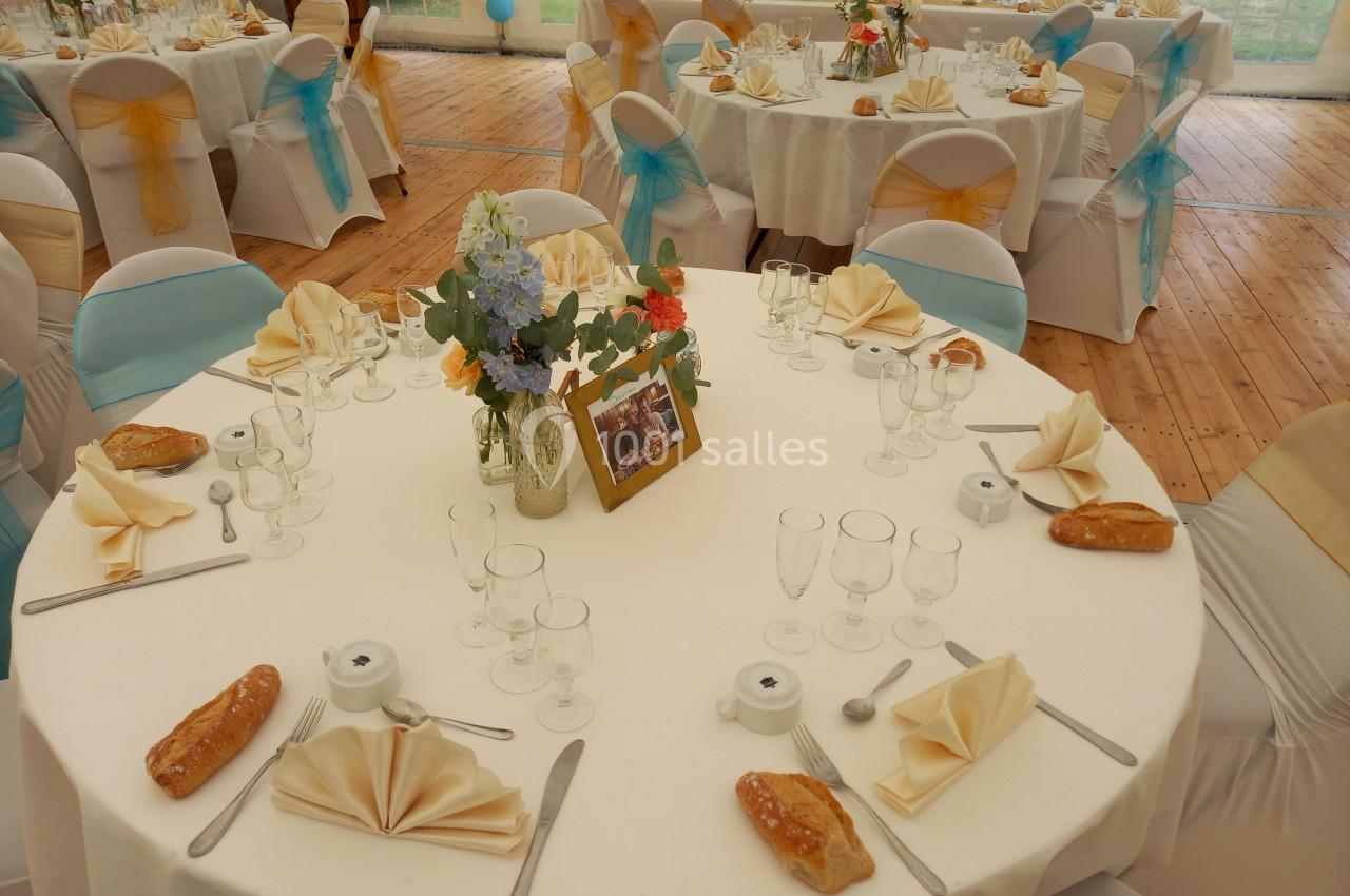 Tables rondes décorées pour un mariage, avec nappes blanches, serviettes pliées, fleurs et couverts disposés.