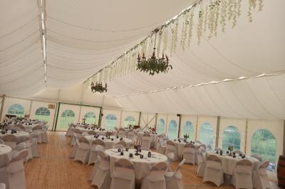 Deux balais déguisés en mariés avec robe et costume, posés devant une tente blanche et un cadre décoratif.