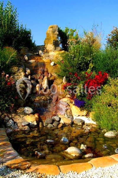 Cascade artificielle entourée de végétation colorée, se déversant dans un petit bassin bordé de pierres.