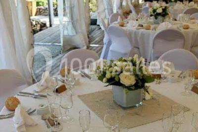 Intérieur d'une tente de réception décorée avec des tables rondes dressées, des chaises blanches et des fleurs.