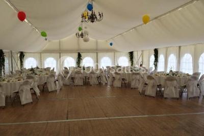 Intérieur d'une tente de réception décorée avec des tables rondes dressées, des chaises blanches et des fleurs.