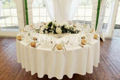 Intérieur d'une tente de réception décorée avec des tables rondes dressées, des chaises blanches et des fleurs.