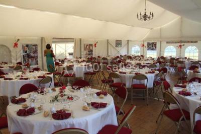 Intérieur d'une tente de réception décorée avec des tables rondes dressées, des chaises blanches et des fleurs.