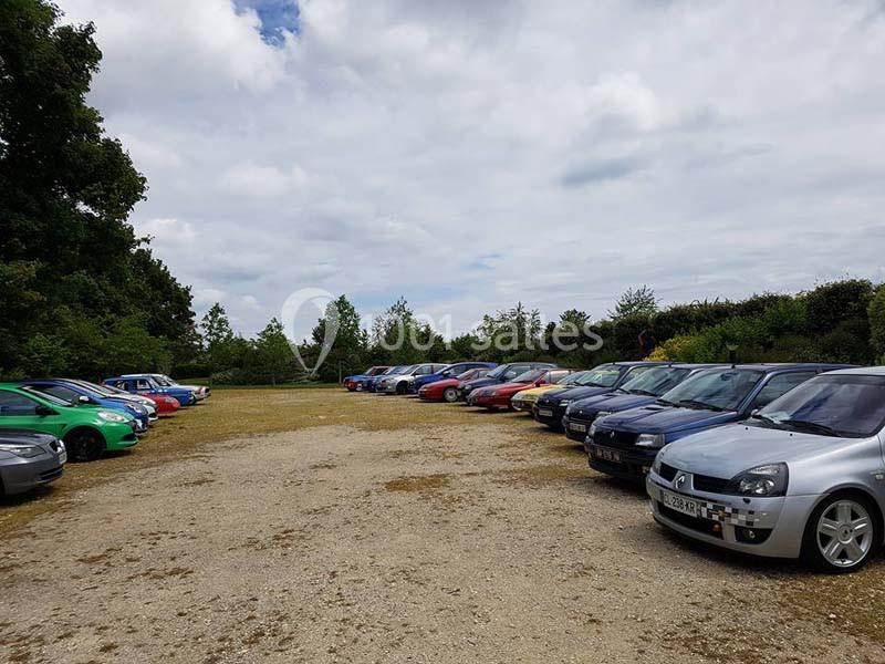 Alignement de voitures colorées stationnées sur un parking en plein air, entouré de végétation et sous un ciel partiellement…