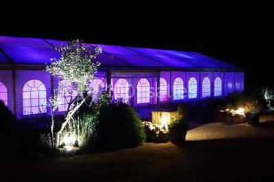 Intérieur d'une tente de réception décorée avec des tables rondes dressées, des chaises blanches et des fleurs.