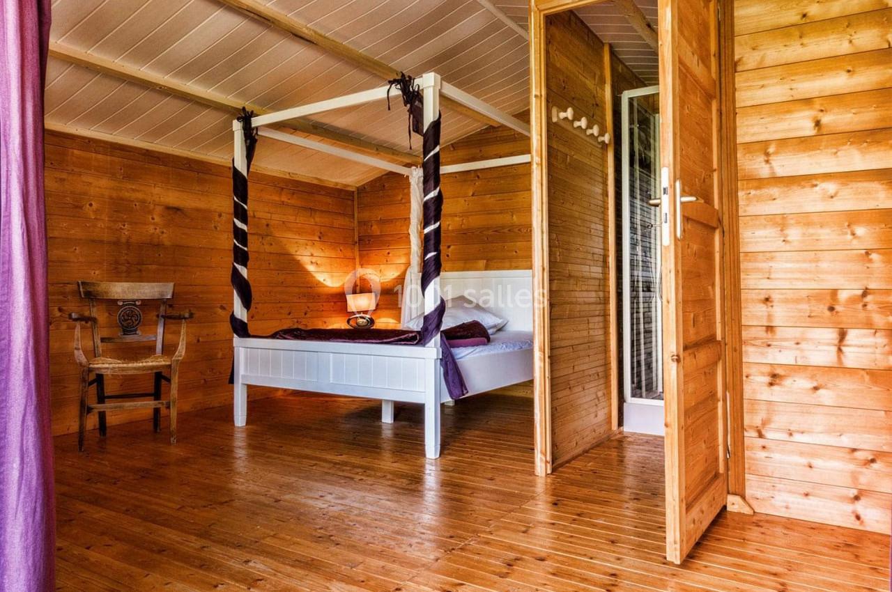 Chambre en bois avec lit à baldaquin blanc, chaise en bois sculpté et lumière naturelle entrant par une fenêtre.
