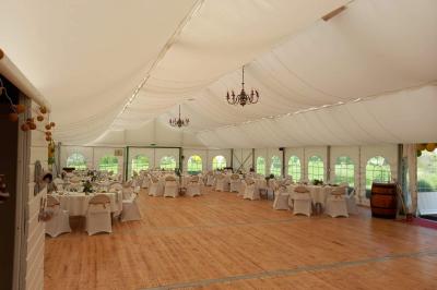 Intérieur d'une tente de réception décorée avec des tables rondes dressées, des chaises blanches et des fleurs.