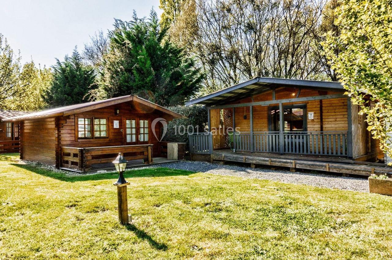 Deux chalets en bois dans un espace extérieur verdoyant, entourés d'arbres et baignés de lumière naturelle.