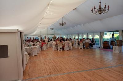 Intérieur d'une tente de réception décorée avec des tables rondes dressées, des chaises blanches et des fleurs.
