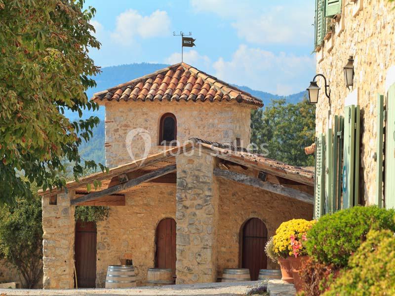 Bâtisse en pierre avec toit en tuiles, entourée de végétation et située dans un cadre rural ensoleillé.