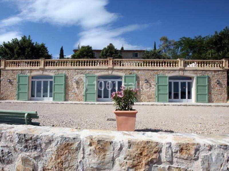 Façade en pierre d'une maison avec volets verts, terrasse en pierre et pot de fleurs au premier plan.