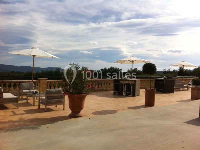 Terrasse spacieuse avec mobilier d'extérieur, parasols blancs, plantes en pot et vue sur un paysage vallonné.