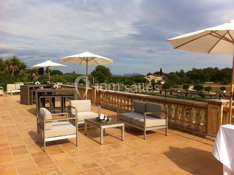 Terrasse spacieuse avec mobilier de jardin moderne, parasols blancs et vue sur un paysage rural.