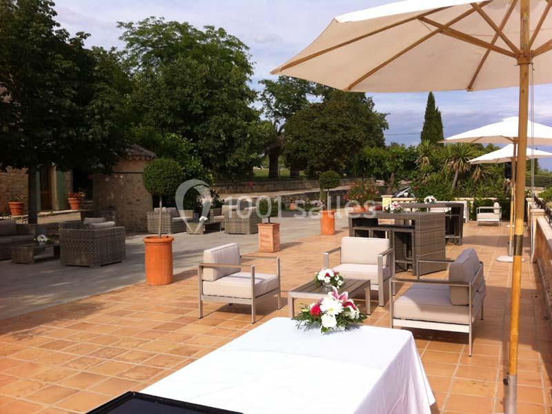 Terrasse aménagée avec des fauteuils, tables, parasols et décorations florales, entourée de verdure.