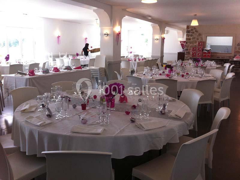Salle de réception décorée avec des tables rondes dressées, nappes blanches et touches de rose.