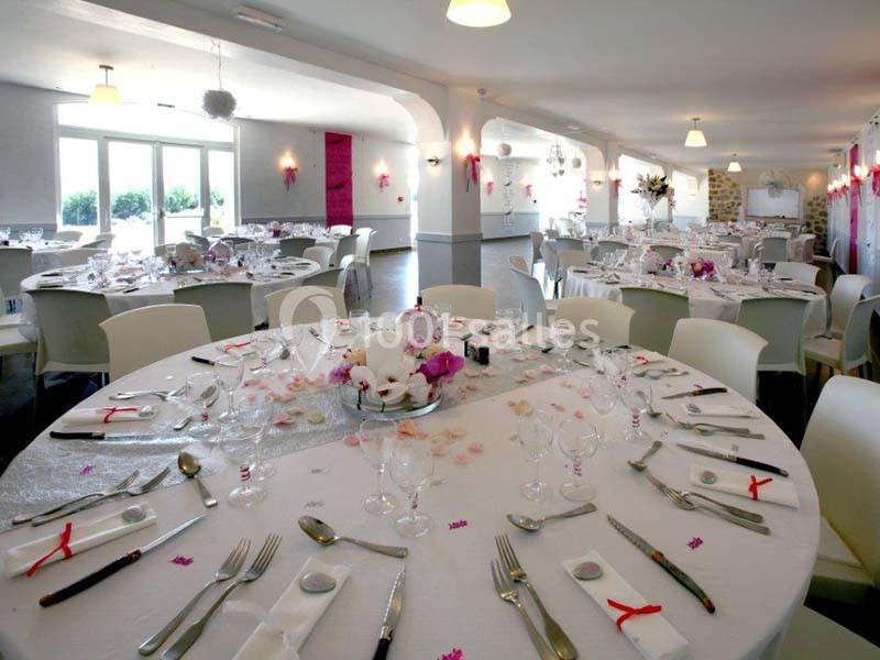 Salle de réception décorée avec des tables rondes dressées, nappes blanches et touches de décoration rose.