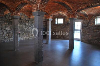 Voûte en briques rouges avec piliers en pierre, sol carrelé gris et mur en pierre apparente.