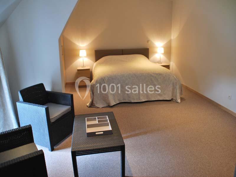 Chambre avec lit double, deux lampes de chevet, fauteuils en osier et table basse dans un intérieur sobre.