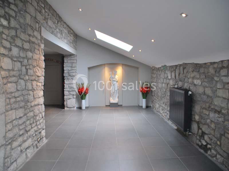 Couloir en pierre avec sol en carrelage gris, statue blanche au fond, éclairage encastré et plantes décoratives.