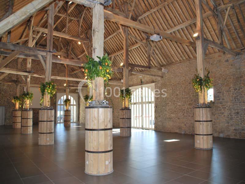 Salle spacieuse avec poutres apparentes, piliers en bois décorés de feuillage et grandes fenêtres laissant entrer la lumière.