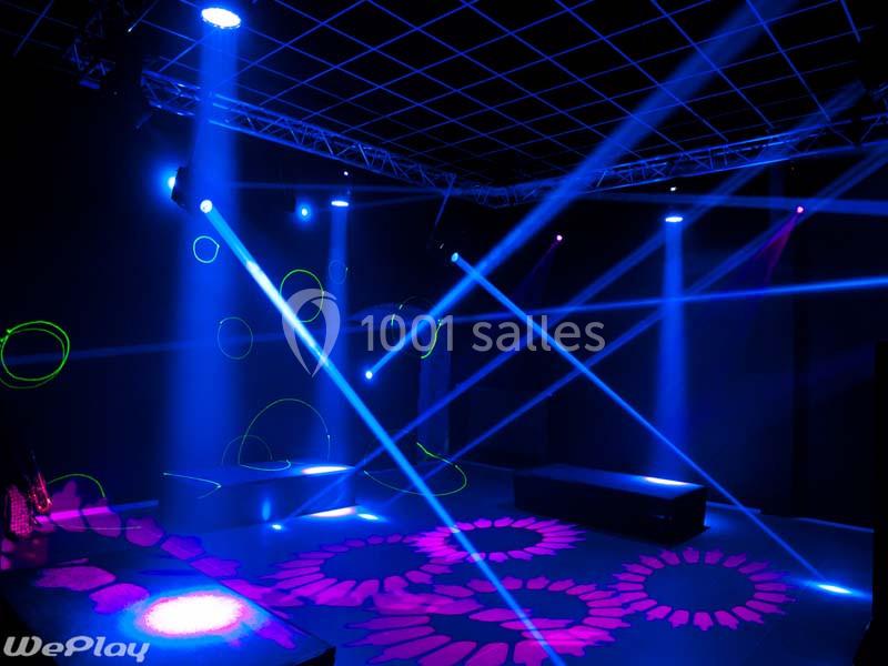 Salle sombre avec éclairage scénique coloré, faisceaux lumineux et motifs projetés au sol.