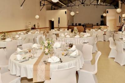 Salle avec des rangées de chaises en plastique beige face à une scène surélevée dans un espace lumineux.
